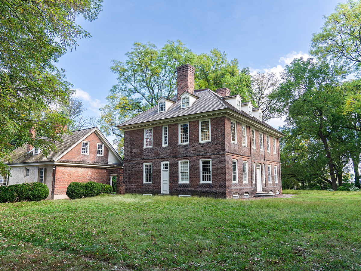 A three story brick building with white windows sits on a grassy lawn surrounded by green trees.