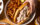 A hand with silver painted nails reaches for half a a cheesesteak on a round plate with crispy French fries and pickle slices. The Wit or Witowski Kielbasa Cheesesteak includes chipped kielbasa with onions and melted American cheese on a long roll.