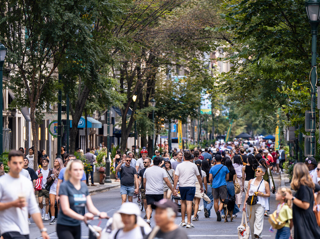 Des groupes de personnes marchent dans une rue sans voiture pendant Open Streets West Walnut. Certaines personnes poussent des poussettes ou promènent des chiens en laisse.