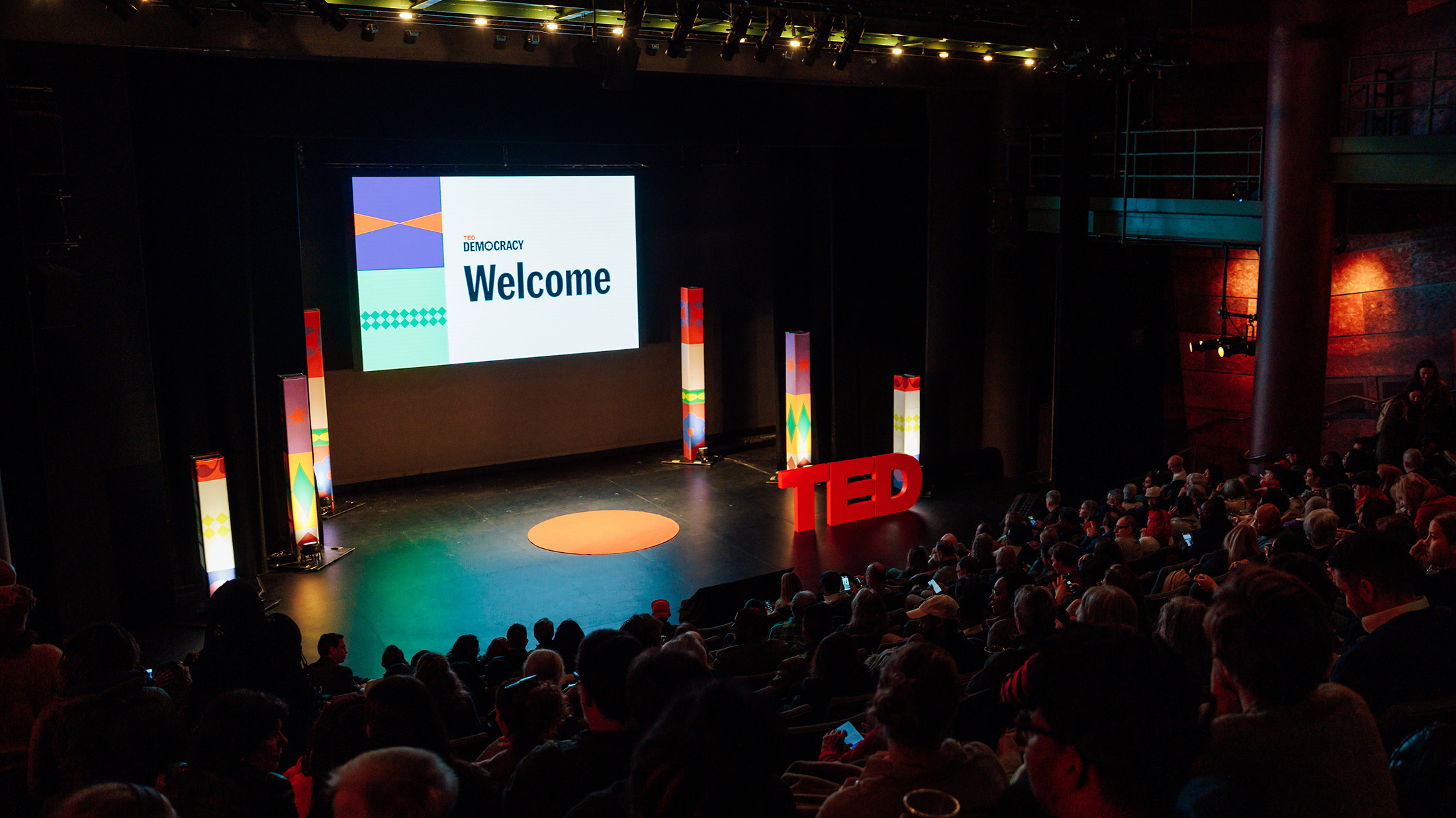 A stage with the words TED on it and a screen behind it in an auditorium with a audience