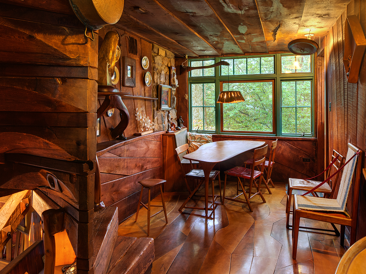 L'intérieur de la salle à manger de l'atelier de Wharton Esherick. La pièce est dotée d'un parquet, de murs et d'un plafond en bois. Une table de salle à manger en bois aux formes irrégulières trône au milieu de la pièce, avec des chaises supplémentaires adossées au mur.