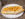 A cheesesteak is displayed on a white round plate on a tabletop. The long roll holds chunks of chicken with cheese whiz on top.