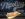 A ribeye cheesesteak topped with an over easy egg, sriracha and smashed tater tots is held up on a plate in front of a chalkboard.