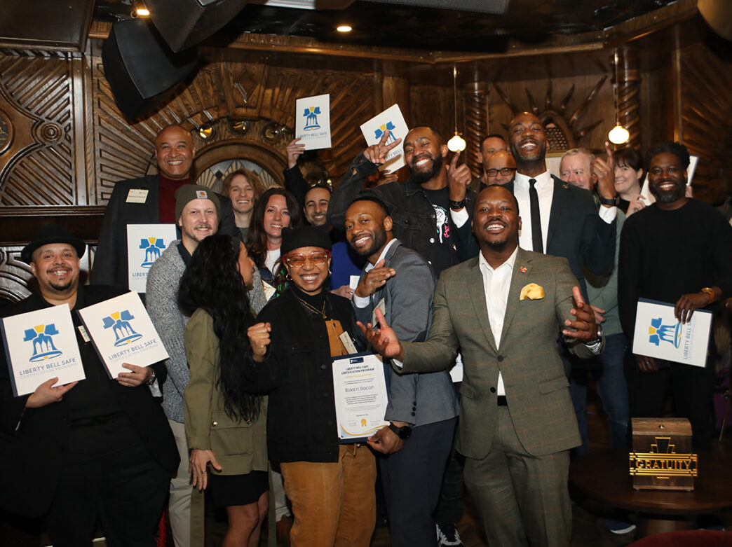 A group of people stand together for a photo at the Liberty Bell Safe Certified Business recognition ceremony. People smile and hold up their certificates.
