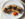 A cheesesteak cut into quarters is displayed on an oval white plate with orange, yellow and red pepper slices.