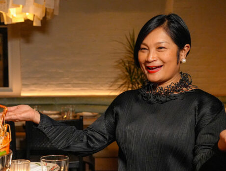 Chef Nok Suntaranon sits at a round wooden table and holds her arms open while presenting a seafood tower at Kalaya.