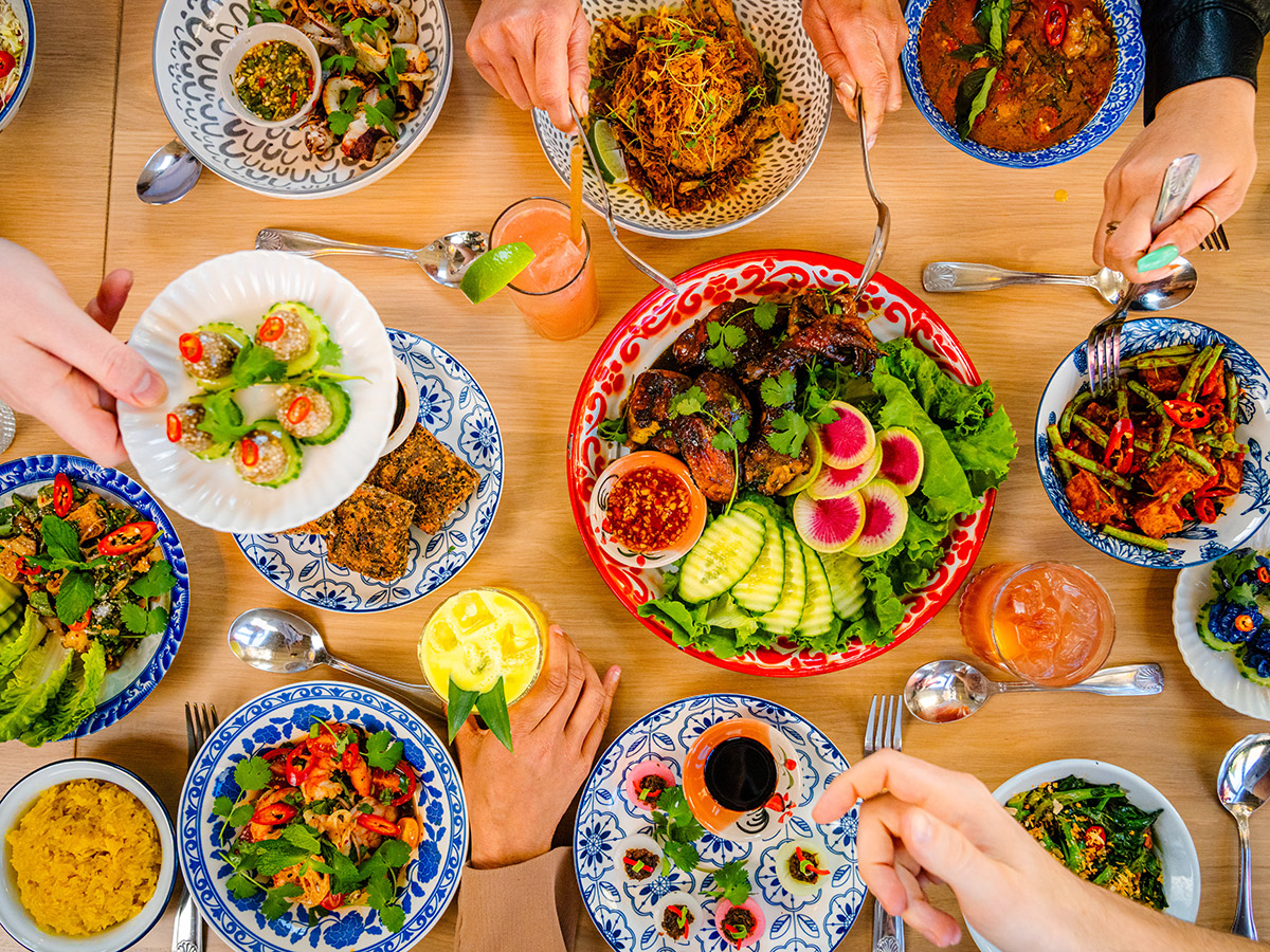 Multiple people dig into a colorful spread of Thai dishes at Kalaya.