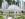 A large, elegant courtyard with symmetrical fountains and trimmed hedges. Power water jets shoot water high into the air while people walk through the garden space.