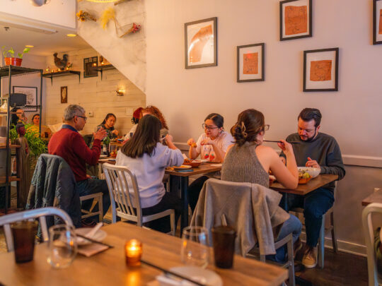 La salle à manger de Mawn est chaleureuse et accueillante. Les clients sont assis à de petites tables en bois et savourent leur repas. Des dessins de poulets sur du papier brun sont exposés dans des cadres sur les murs.