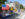 Performers in bright yellow and blue uniforms march beside a colorful float decorated with a large American flag and a “Happy Birthday America” sign.
