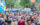 Crowds of people walk down Walnut Street. Someone on the left carries and arrangement of blue, white and yellow balloons, and vendor tents and food trucks are set up in the street.