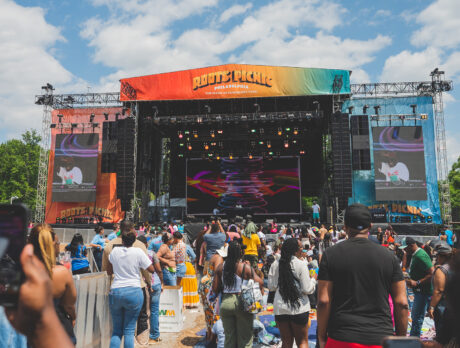 A large crowd gathers in front of the colorful Roots Picnic main stage, where a performer is on stage performing.
