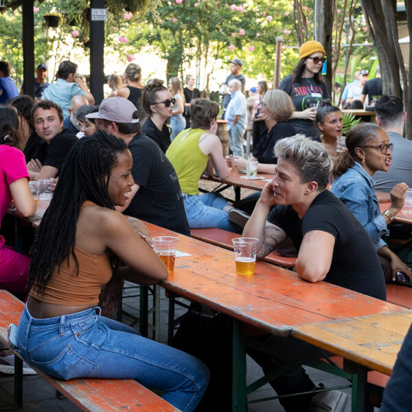 People gather around long picnic tables under string lights and greenery at the PHS Pop Up Garden on South Street.
