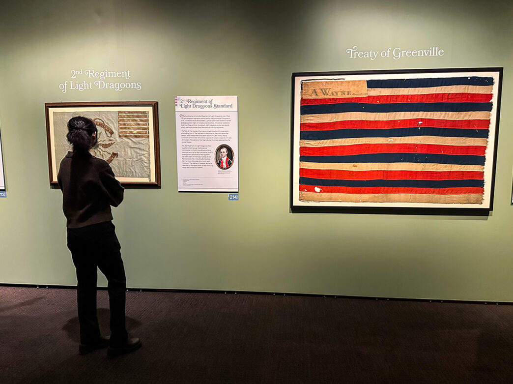Une personne regarde les drapeaux exposés dans des cadres sur le mur d'une galerie au Museum of the American Revolution.