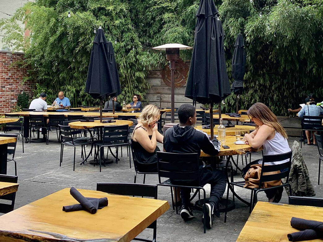 Diners relax at wooden tables in the leafy garden at Front Street Café, surrounded by lush bamboo and shaded by black umbrellas.