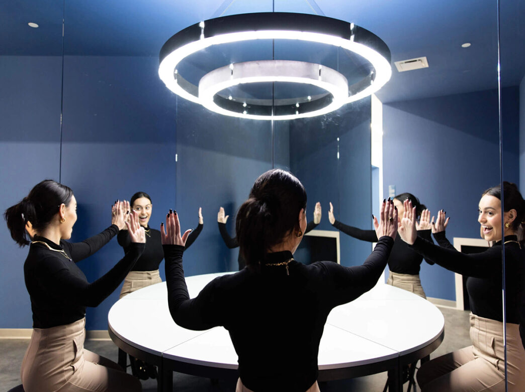A visitor smiles and interacts with her own reflections in a mirrored room at the Museum of Illusions, where cleverly angled glass panels create a playful, infinite illusion.