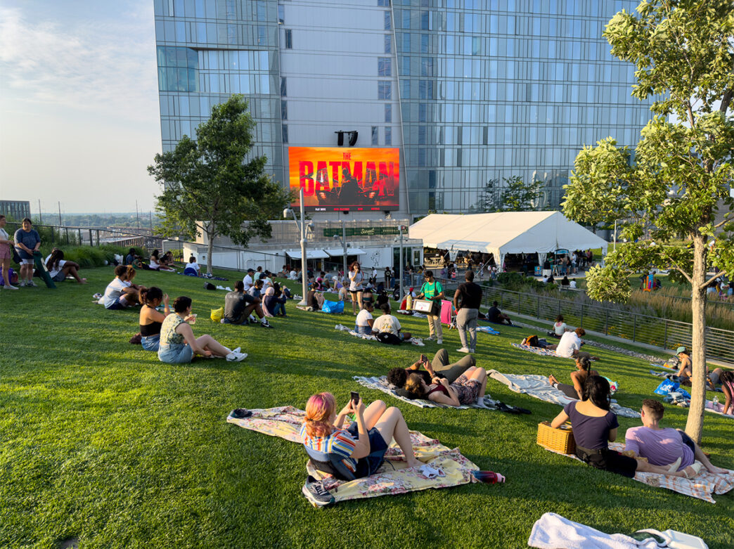 People relax on blankets and lawn chairs during an outdoor screening of The Batman at Sunset Social’s rooftop green space.