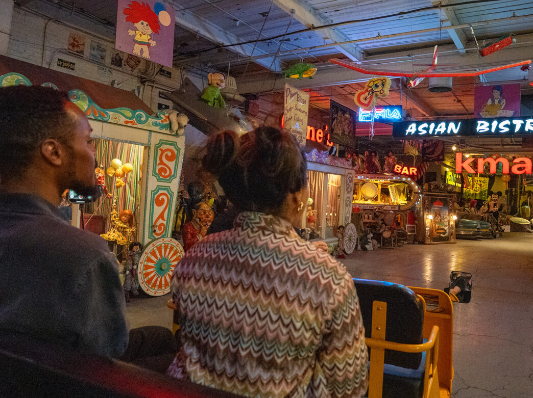 Two visitors ride through a room filled with color vintage signs, animatronics and memorabilia on a guided tram tour at the American Treasure Tour Museum.