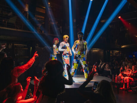 Three performers wearing colorful pants dance on stage at Fabrika while the crowd cheers and takes photos.