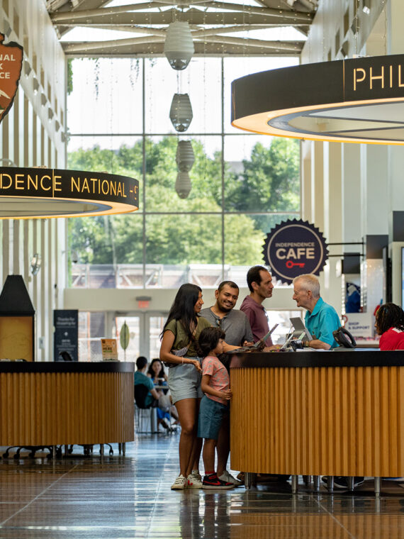 People stand at an information desk and speak to a staff member in Philadelphia Independence Visitor Center.
