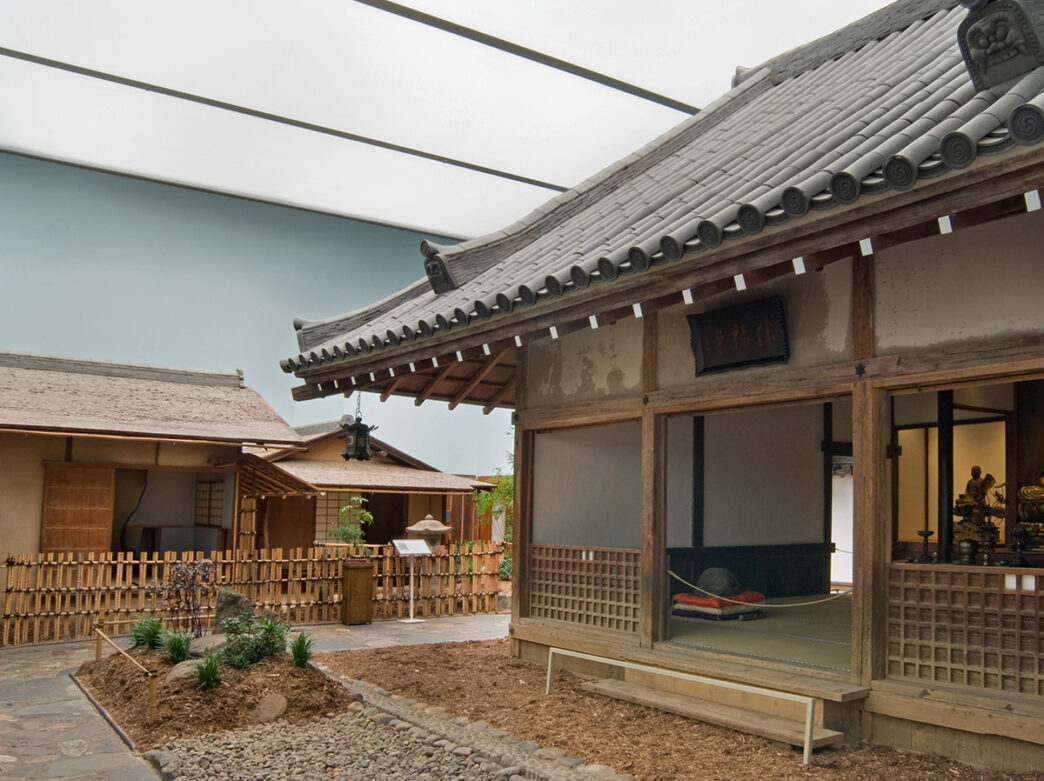 A traditional Japanese tea house constructed of bamboo and a stone garden on display in a brightly lit exhibit at the Philadelphia Museum of Art.