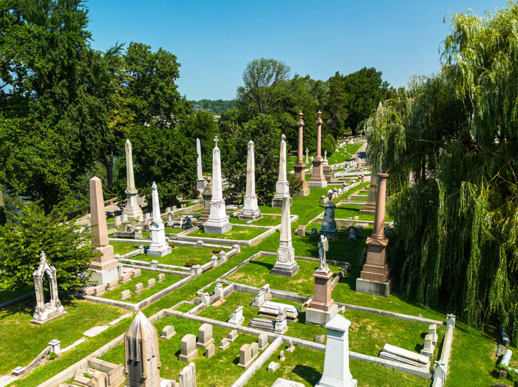 Aerial view of headstones, pillars, and green trees at Laurel Hill Cemetery on a summer day.