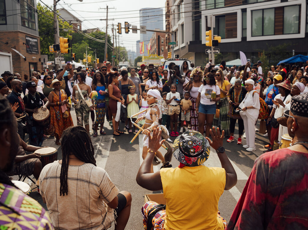 Une foule de spectateurs regarde une danseuse et un groupe de percussionnistes se produire au festival de rue ODUNDE.