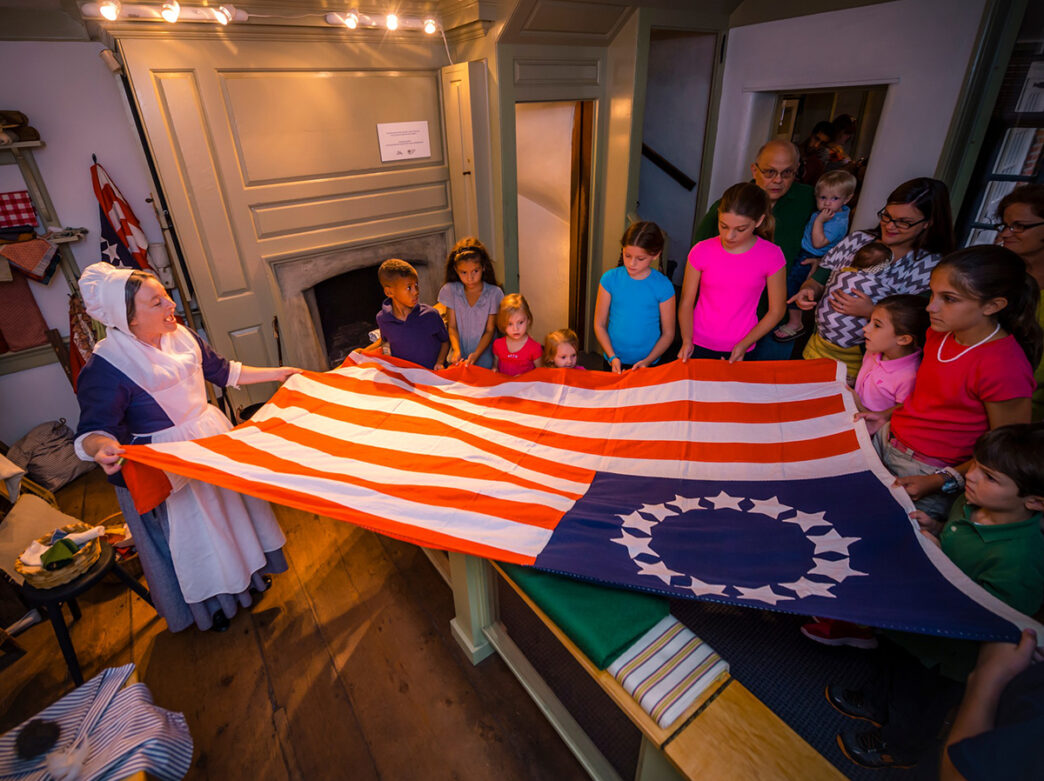 A Betsy Ross reenactor holds an American Flag with visitors inside the Betsy Ross House.