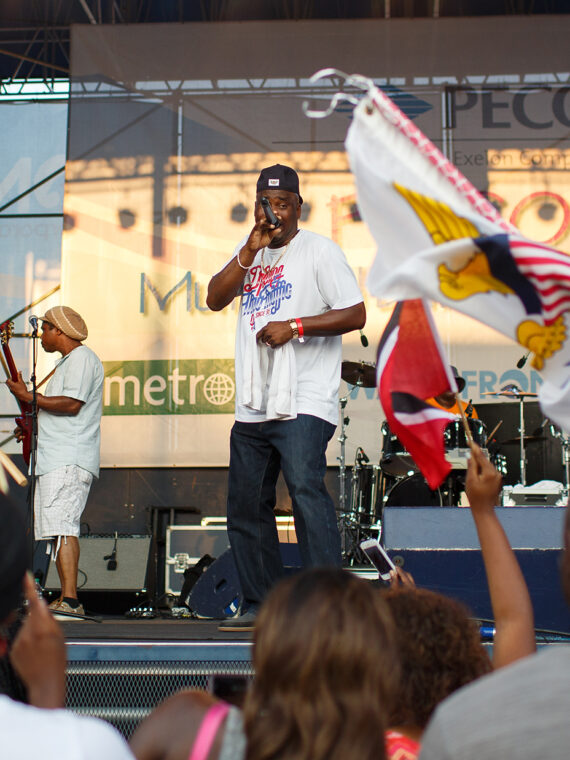A artist performs on stage at the Caribbean Festival while audience members wave colorful Caribbean flags and dance along to the music.