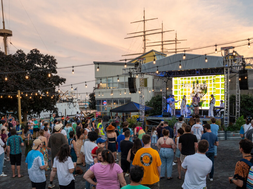A crowd gathered in front of performers on a stage during a concert at Spruce Street Harbor Park.