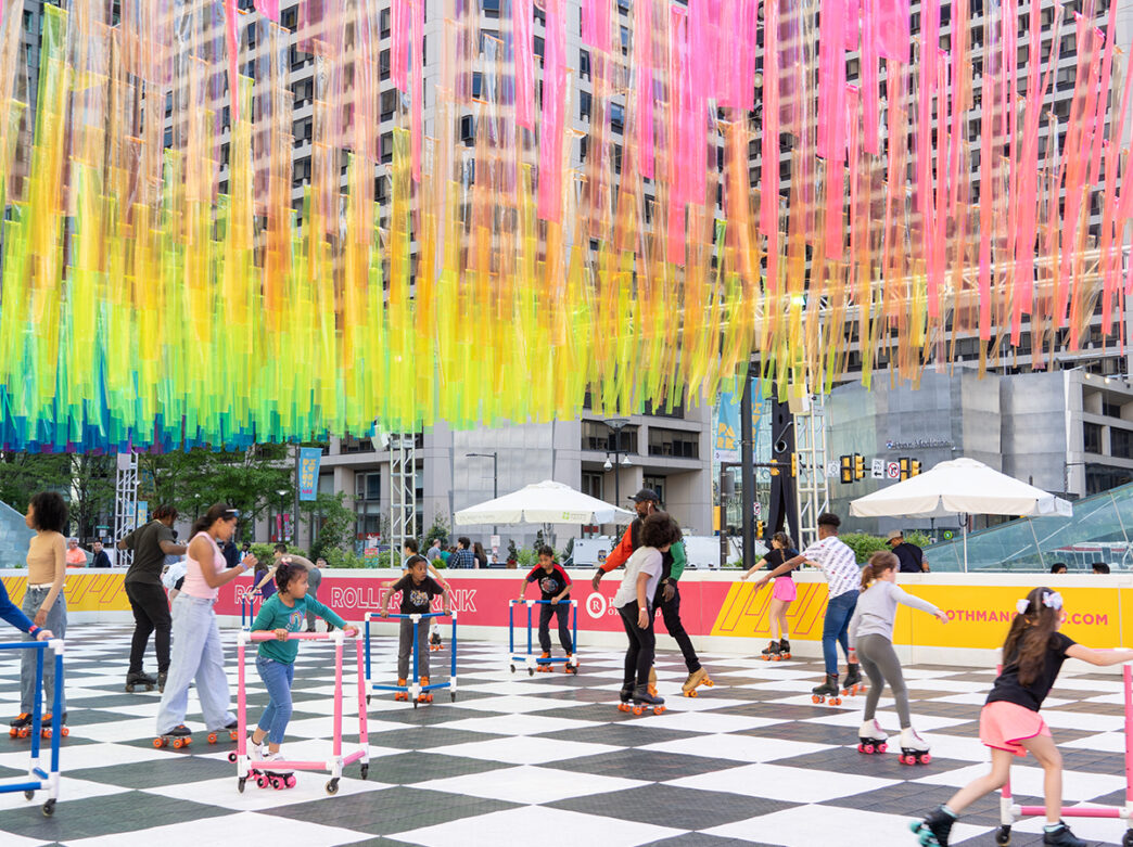 Children rollerblade on a black and white roller rink at Philadelphia City Hall. Colorful streamers hang from above.
