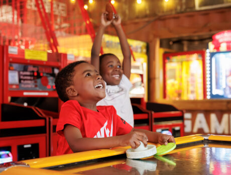 Surrounded by bright lights and colorful carnival games, two young boys laugh while playing air hockey at a Summerfest's lively arcade.