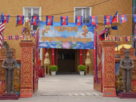 The exterior the Preah Buddha Rangsey Temple in Philadelphia, with a red and orange gate entrance decorated with bronze and gold statues.