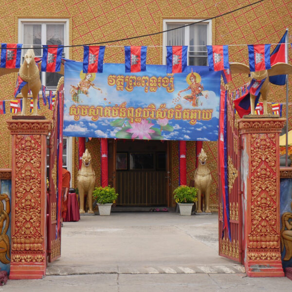 The exterior the Preah Buddha Rangsey Temple in Philadelphia, with a red and orange gate entrance decorated with bronze and gold statues.