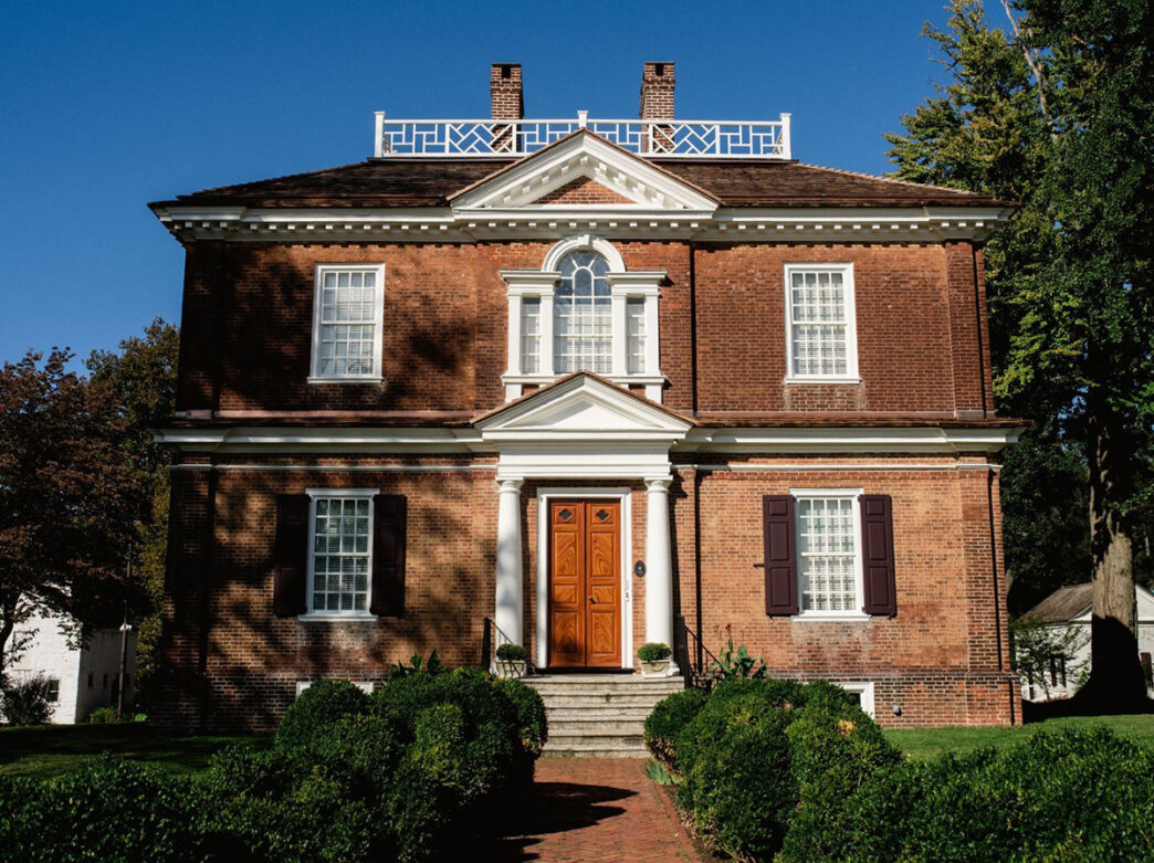 A red brick Georgian-style mansion with a symmetrical facade, white trim and a brick path leading to the main door.