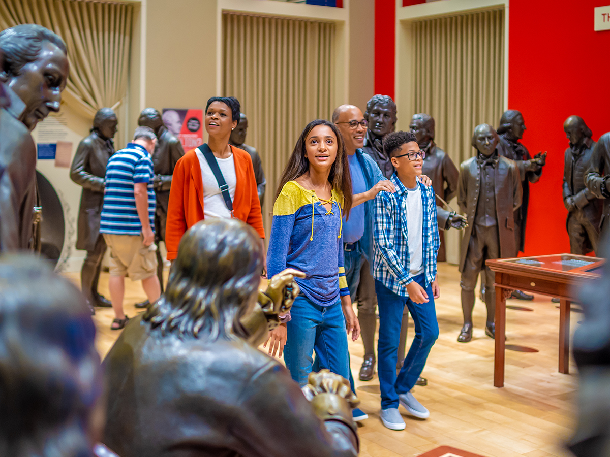 A family walks through a room of life-sized bronze statues of the Founding Fathers at the National Constitution Center.
