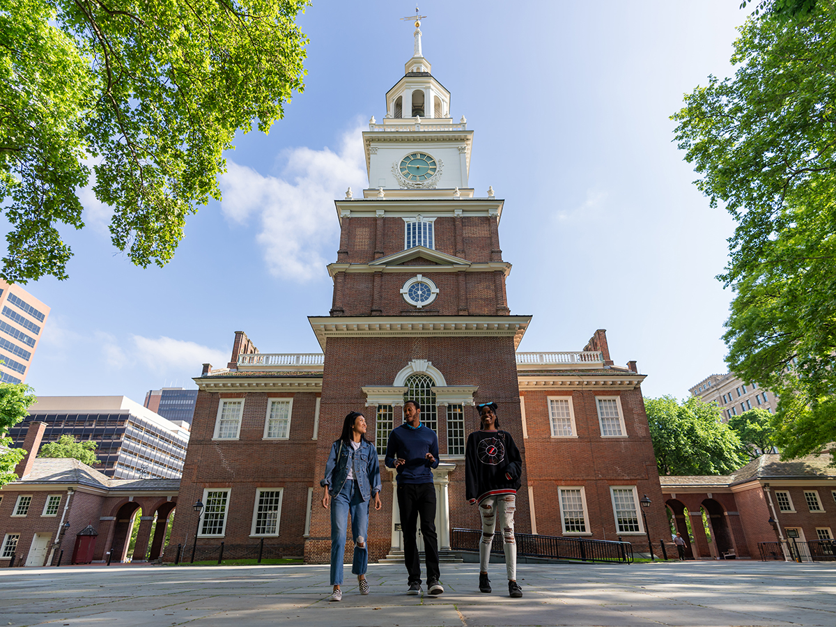 Three people walk with the back of Philadelphia's Independence Hall in the background.