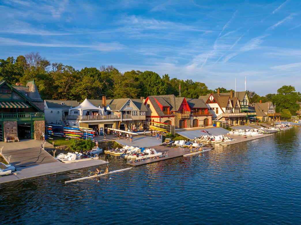 Vista aérea de casas de barcos do século 19 ao longo do rio Schuylkill, na Filadélfia. Um barco a remo para duas pessoas está no rio.