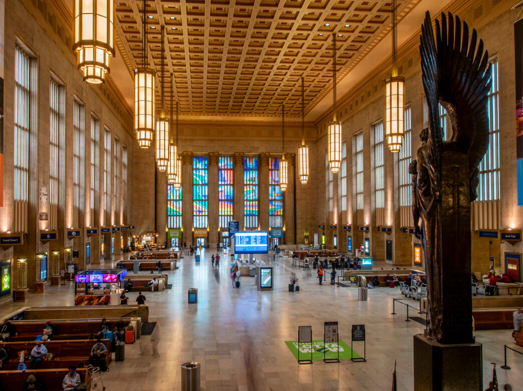 Interior of William H. Gray 30th Street Station Amtrak station in Philadelphia. The station features tall ceilings, hanging pendant lights and a large bronze statue.