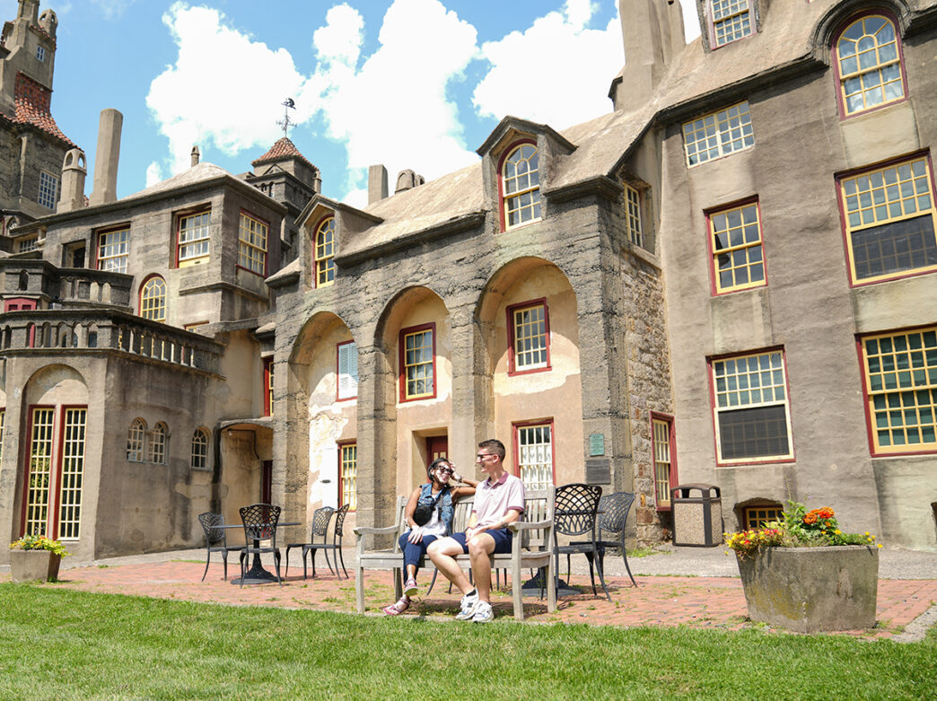 Duas pessoas sentadas em um banco em um dia claro e azul, com o Fonthill Castle ao fundo.