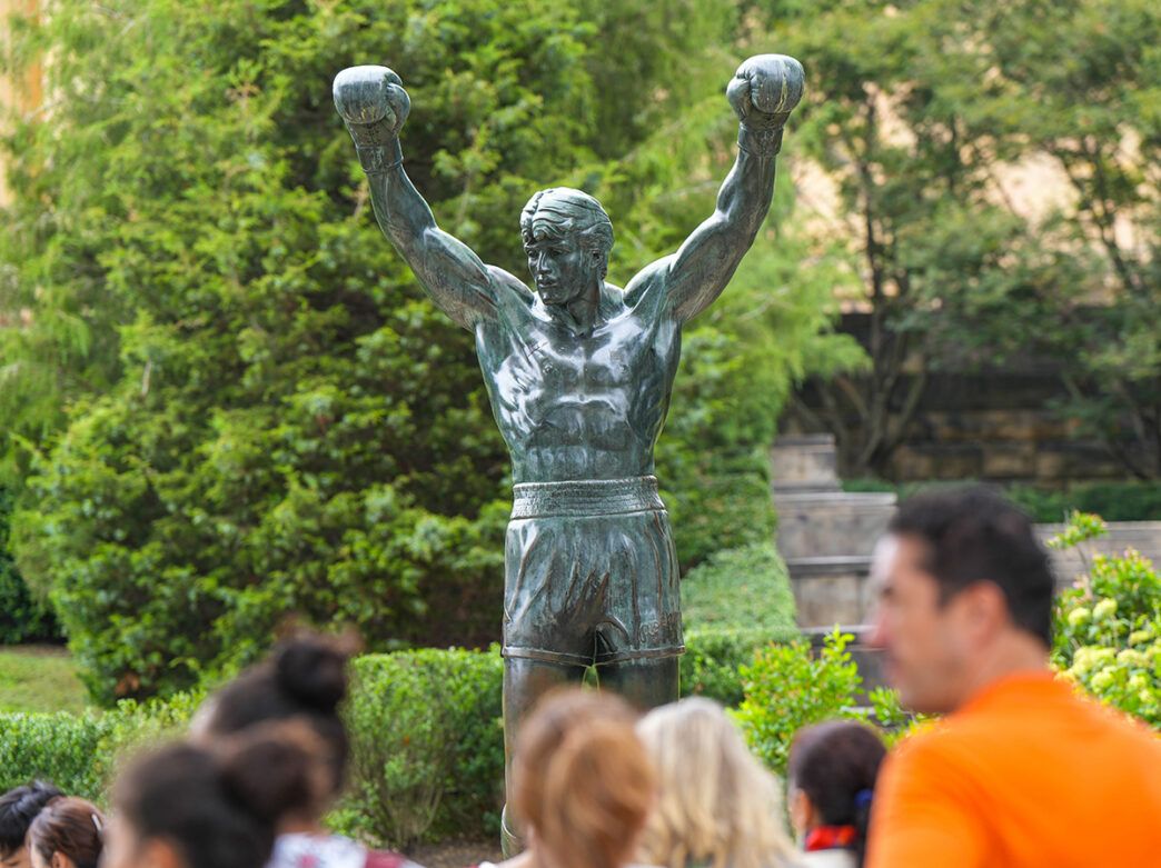 La statue de Rocky avec une foule de personnes légèrement floue au premier plan.