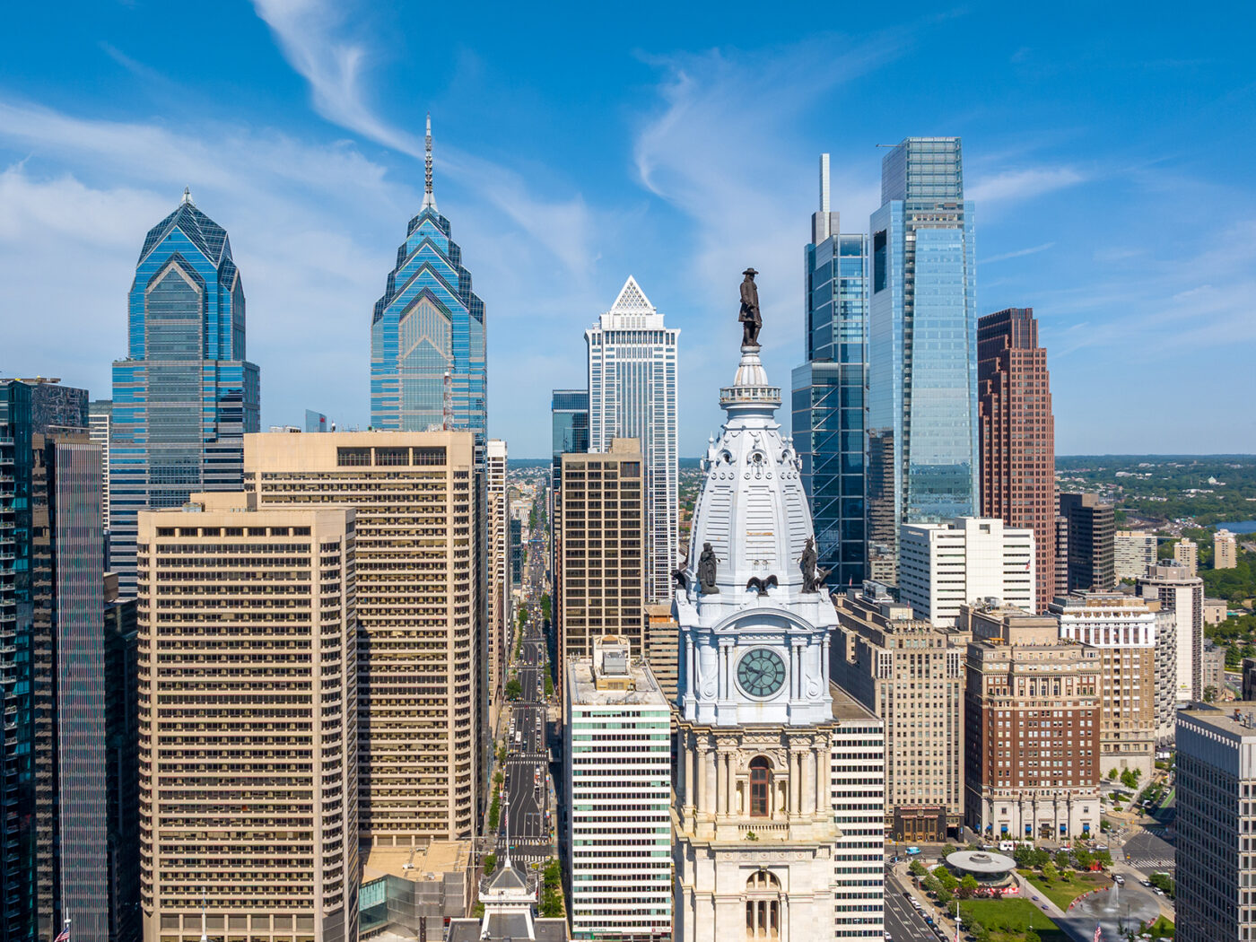 La silhouette du centre-ville de Philadelphie, avec la statue de William Penn au sommet du City Hall, entourée de gratte-ciel modernes en verre sous un ciel bleu éclatant.