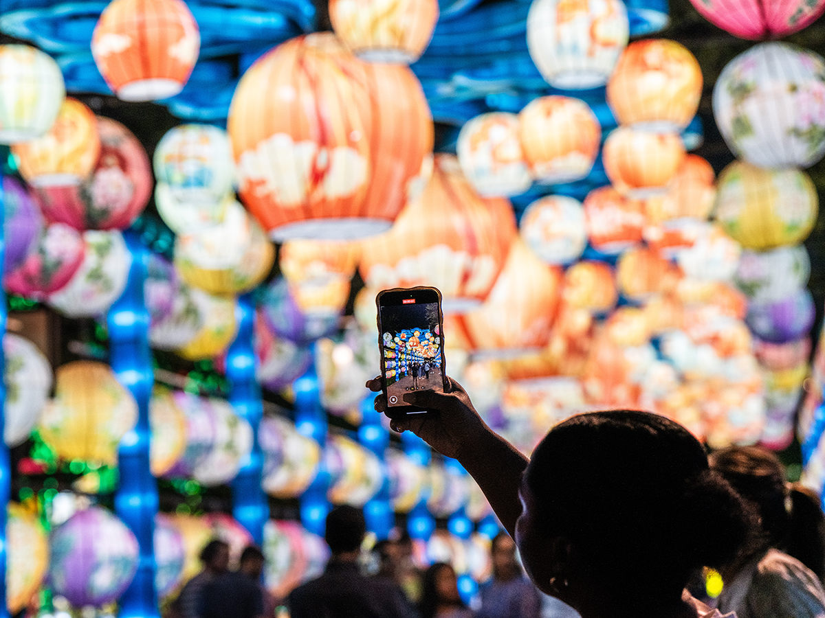 Une personne lève son téléphone pour prendre une photo des lanternes colorées et lumineuses suspendues au-dessus de sa tête dans un tunnel lors du Festival des lanternes chinoises.