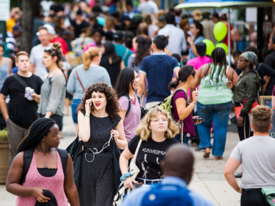 Una multitud bulliciosa llena la avenida Baltimore durante el Dollar Stroll. La gente socializa, camina y se detiene para tomar algo.