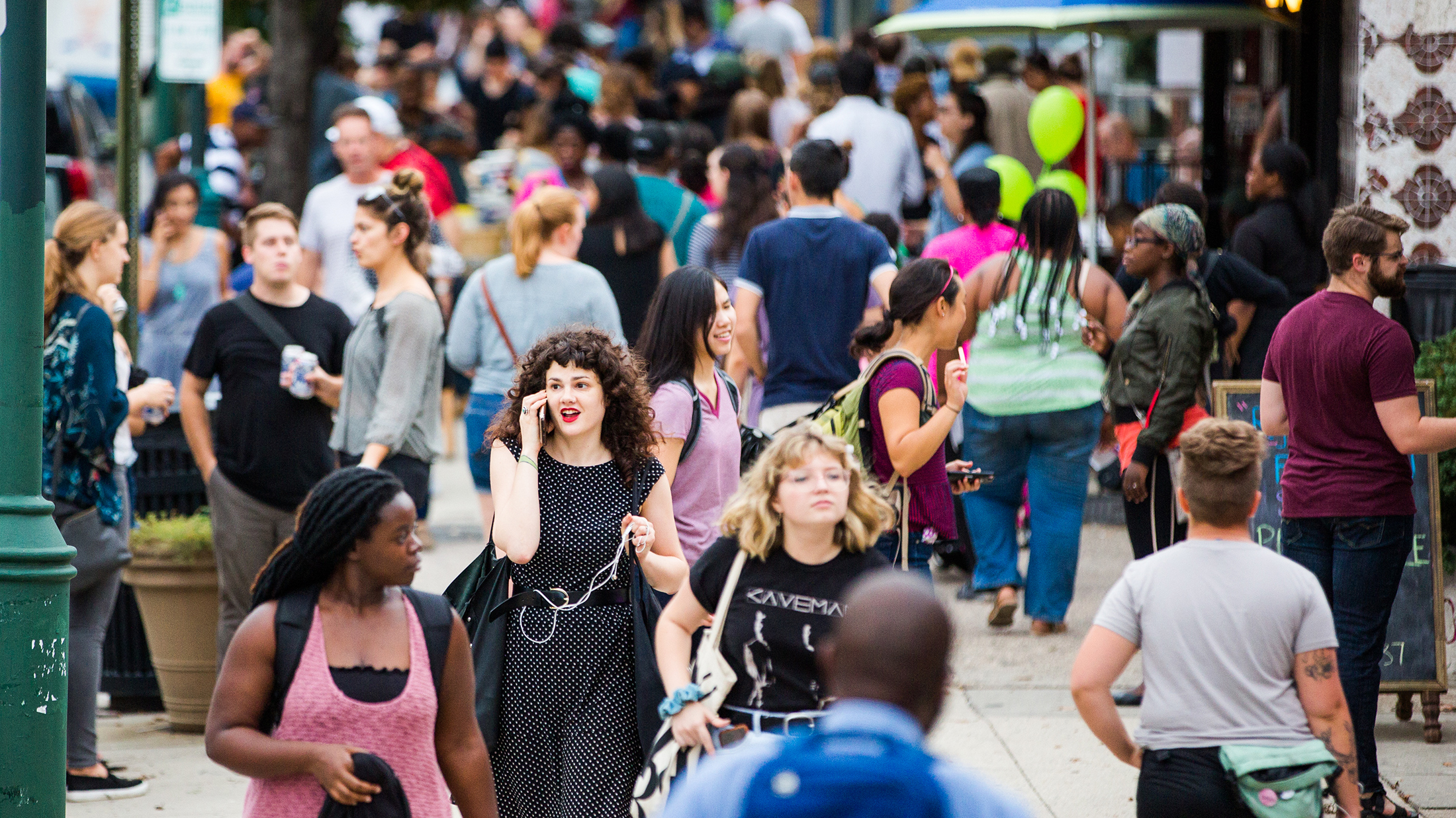 A bustling crowd fills Baltimore Avenue during the Dollar Stroll. People socialize, walk and stop for drinks.