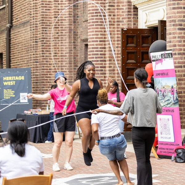 A group of women jump rope together during a Juneteenth event outside the Penn Museum. Onlookers cheer and capture the fun on camera.