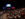 A packed theater audience sits facing a brightly lit stage, where a screen reads "Welcome" alongside TED Democracy branding and colorful pillars.