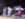 Three vocalists in shimmering silver, white and pink outfits sing and dance on stage backed by a full band.