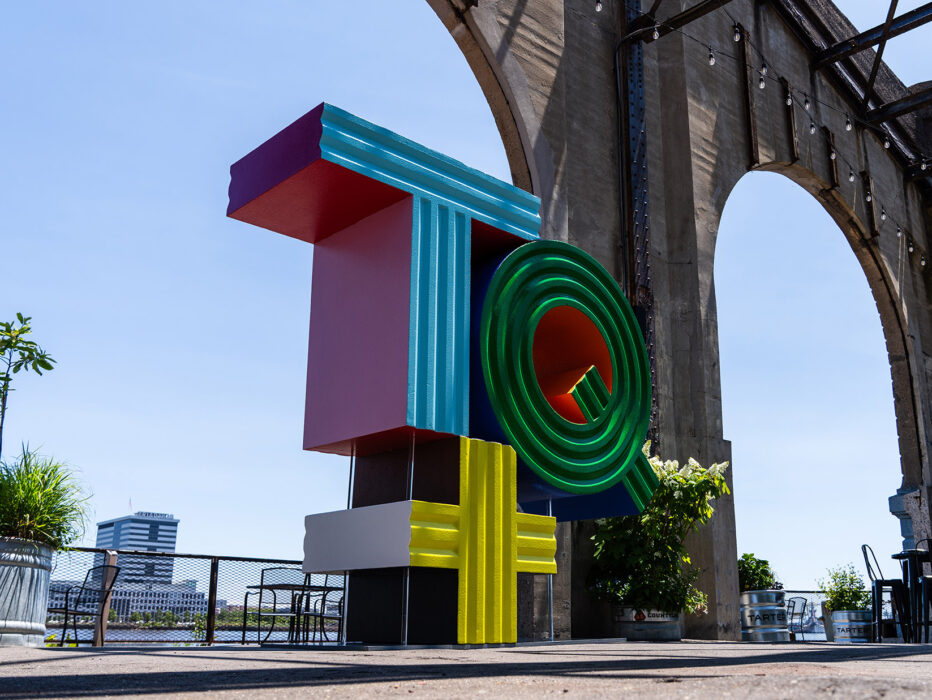 A multi-colored sculpture that says "TQ+" stands outdoors.