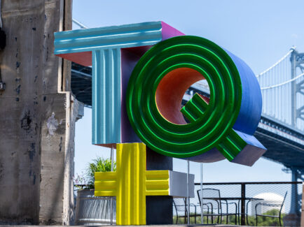 A multi-colored sculpture that says "TQ+" stands outdoors. The Delaware River and Benjamin Franklin Bridge are visible in the background.